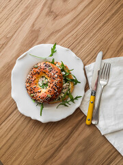 Bagel sandwich with tuna eggs salad and arugula - delicious breakfast, snack on a wooden background, top view