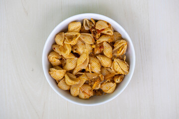 Delicious shell pasta in a white bowl on wooden background. Top view of tasty conchiglie rigate pasta. 