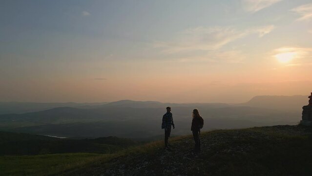 Fantastic aerial view of scenery at sunset from a mountain peak and young people silhouettes celebrating successful climb with high five gesture.