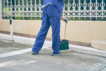 A janitor with a broom sweeps the area on the street. A man in a work uniform works during a...