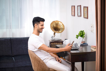 Happy Smiling Man In White Outfit Reading Message On Phone While Working At Home Office
