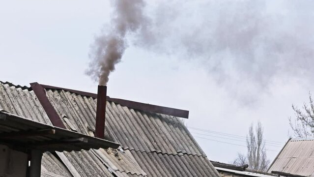 Black smoke coming out from rustic bathhouse chimney steel pipe, the concept of heating with low quality coal or rags.