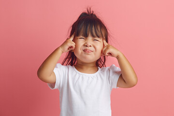 Little Asian girl of three years squinting is struggling to concentrate or remember important information, had a bad memory, has a thoughtful expression standing over pink isolated background. - 795238106