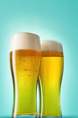 Two glasses with foamy beer on light blue background.