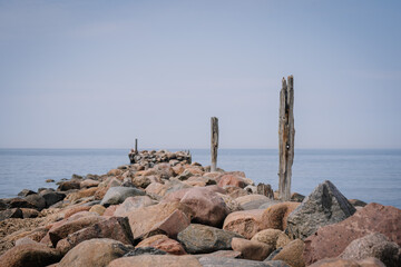 Tuja, Latvia - August 14, 2023 - Rocky jetty with weathered wooden posts leading into calm sea, clear sky.
