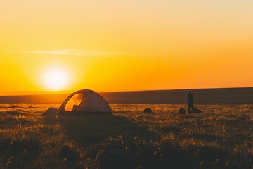 Lone camper against sunrise backdrop, tent pitched on grassy knoll