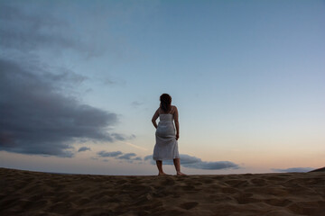 Young woman stands with her back on a sand dune