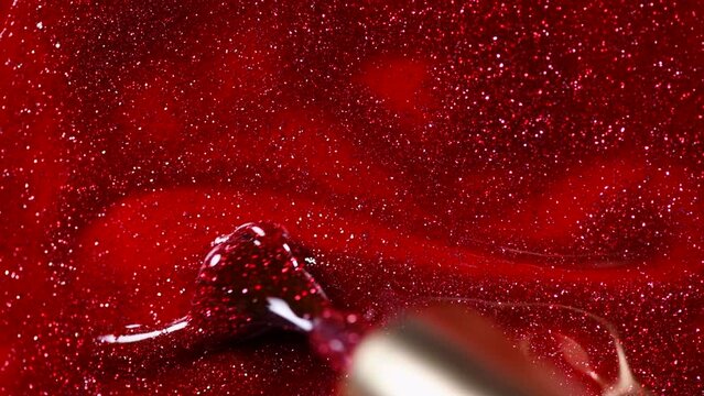 Red glitter nail polish UV gel background with brush. Nailpolish liquid surface, red shellac UV gel brush, varnish, manicure concept. Manicure salon, shellac texture background, backdrop. Top view. 