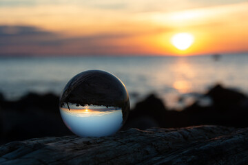 Glass ball  lies on  wood in which the beach and the sea are reflected