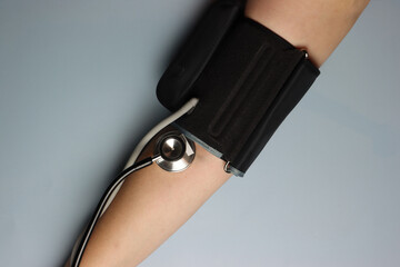 Woman’s arm with a blood pressure equipment and stethoscope. Top view in a grey background 