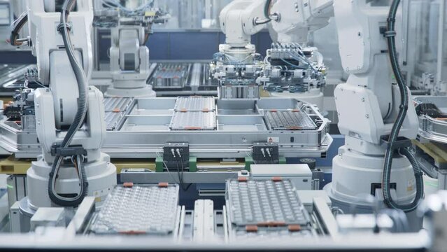 Automated Production Line with White Robotic Arms at Bright Factory. Robot Arms Assemble Lithium-Ion EV Battery Pack for Automotive Industry. Electric Car Smart Manufacturing Line