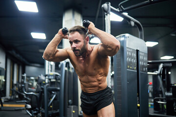 Young bearded man with strong abs, pulling weights, training in gym. Handsome determined guy...