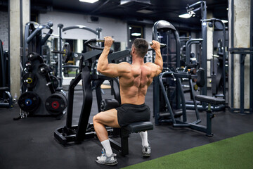 Fototapeta na wymiar Attractive muscular man doing exercise with training apparatus in sports gym. Back view of strong unrecognizable male athlete with bare torso, building muscles indoors. Sport, bodybuilding concept.