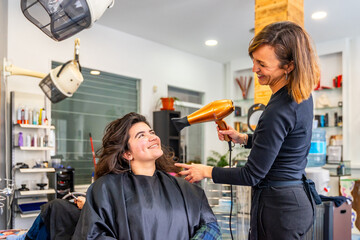 Complicity between hairdresser and customer while drying the hair - obrazy, fototapety, plakaty