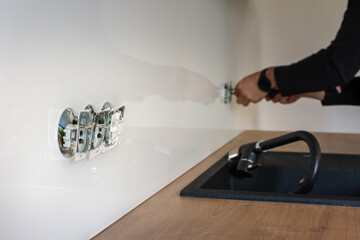 Detail of unfinished socket in glass backsplash, electrician's hand in the background, building a new modern kitchen - obrazy, fototapety, plakaty