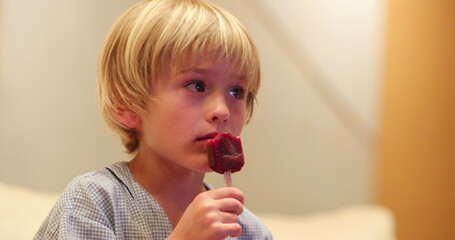 Small boy eating ice cream dessert while watching TV screen at home after dinner
