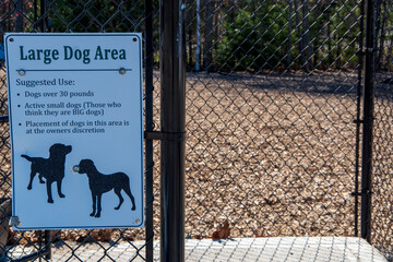 entrance to a dog park, sign on chain link fence and wood chips for a soft surface
