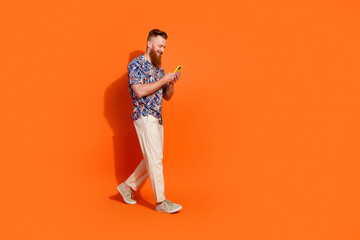 Full length photo of dreamy cute guy dressed print shirt texting device walking empty space...
