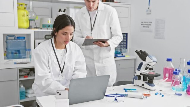 A man and woman in white lab coats working together in a science laboratory filled with research equipment