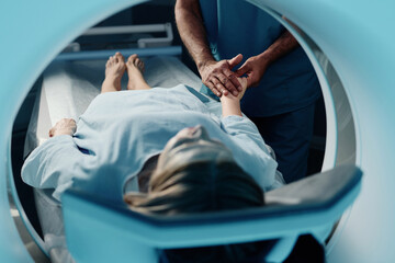 Selective focus shot of unrecognizable doctor holding hand of mature Caucasian woman before CT scan procedure in modern clinic - Powered by Adobe