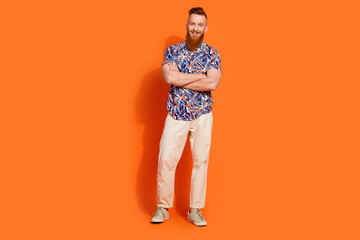 Full size photo of pleasant cool man wear stylish shirt white pants holding arms crossed smiling isolated on orange color background