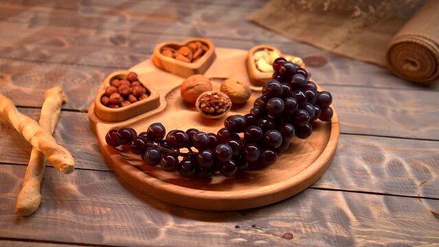 A wooden plate is displayed, featuring an assortment of fresh grapes and nuts. The camera captures the vibrant colors and textures of the fruit and nuts arranged on the plate.