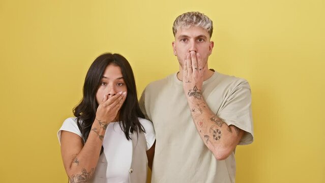 Beautiful couple's silence speaks volumes, shocked expression of fear over a mistake covered by hands-on-mouth. stunned, they stand isolated on yellow background, their silent love echoing.