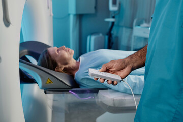 Unrecognizable radiographer holding controller turning on MRI scanner for mature Caucasian female patient, copy space - Powered by Adobe