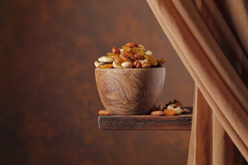 The mix of various nuts and raisins in a wooden bowl on a brown background.