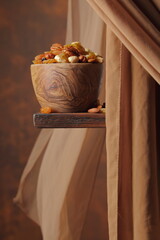 The mix of various nuts and raisins in a wooden bowl on a brown background.