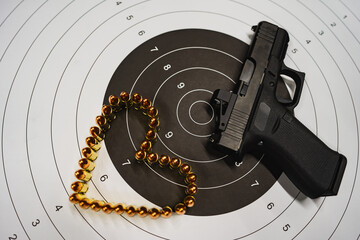 Firearm, modern 9mm compact pistol with red dot, paper target and heart made of cartridges.