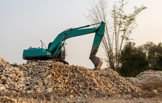 A low-angle view of a green backhoe parked on a pile of granite rubble.