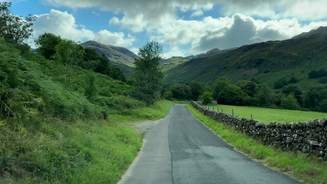 Car front view driving down the narrow road to the bottom of Eskdale valley over River Esk bridge before climbing up to Hardknott Pass in Lake District mountains, United Kingdom.
