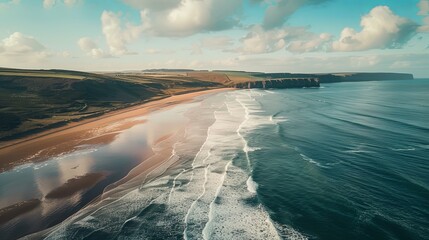 A stunning aerial shot of a boundless sea with gentle waves rolling towards the shore, bordered by sandy beaches and distant coastal cliffs, - obrazy, fototapety, plakaty