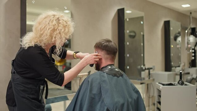 A hairdresser cuts a Caucasian man in a beauty salon. A barber works doing a boy's hair. High quality 4k footage