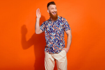 Photo of dreamy friendly guy dressed print shirt waving arm hi looking empty space isolated orange color background