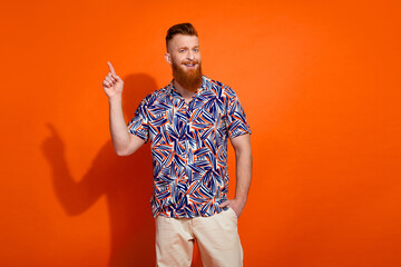 Photo of cheerful positive guy dressed print shirt showing finger empty space isolated orange color background
