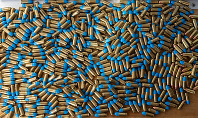 Texture detail of a pile of 9mm bullets on a wooden table, it is reloaded ammunition with a blue...