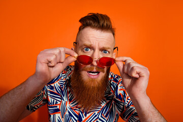 Portrait of astonished man with trendy haircut wear print shirt touch glasses look at discount isolated on vivid orange color background