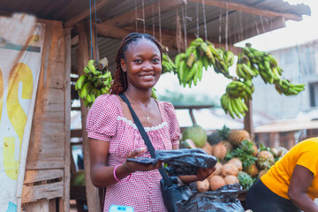Attractive Young African Female Fruit Vendor Holding Nylon Pack at Colorful Fruit Stand