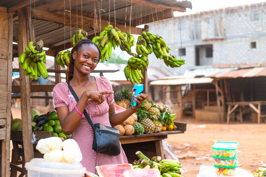 Confident African Saleswoman Pointing at POS Terminal at Fruit Stand