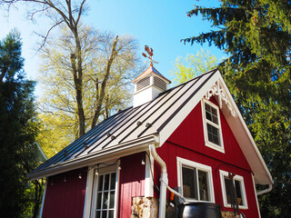 Copper rooster weathervane and cupola on red shed or barn with dark metal roof