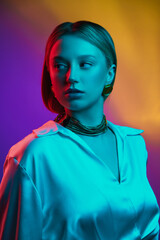 Portrait of modern elegance, featuring female model in silk blouse and golden jewelry against gradient background in neon light Concept of modern fashion, trendy style, beauty, youth culture