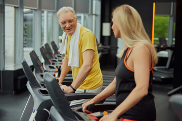 Fototapeta na wymiar Two cheerful seniors, man and woman in sportwear working out together on gym machines. Concept of sport, active seniors in modern life, healthy lifestyle, fitness. Ad