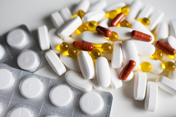 A pile of white and yellow pills and capsules and blistered tablets
