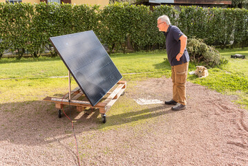 Senior man with photovoltaic solar panel in the garden.