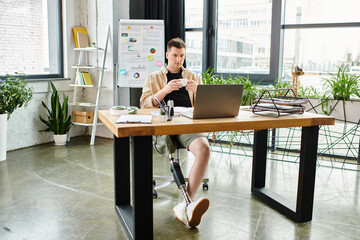 A handsome businessman with a prosthetic leg working diligently at a desk using a laptop.