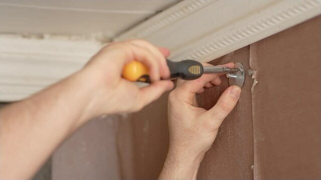 Handyman using screwdriver to install mechanism for new blinds. Close up man screws iron screw or bolt into previously drilled holes in wall to hang cornice in old apartment