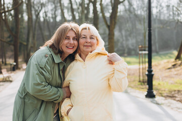 Happy loving older mature mother and daughter laughing embracing, caring young woman embracing senior middle aged mom spending time together on nature background. Woman with elderly mother in park