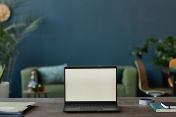 Minimal background image of open laptop on table in office with blank screen against teal blue wall...